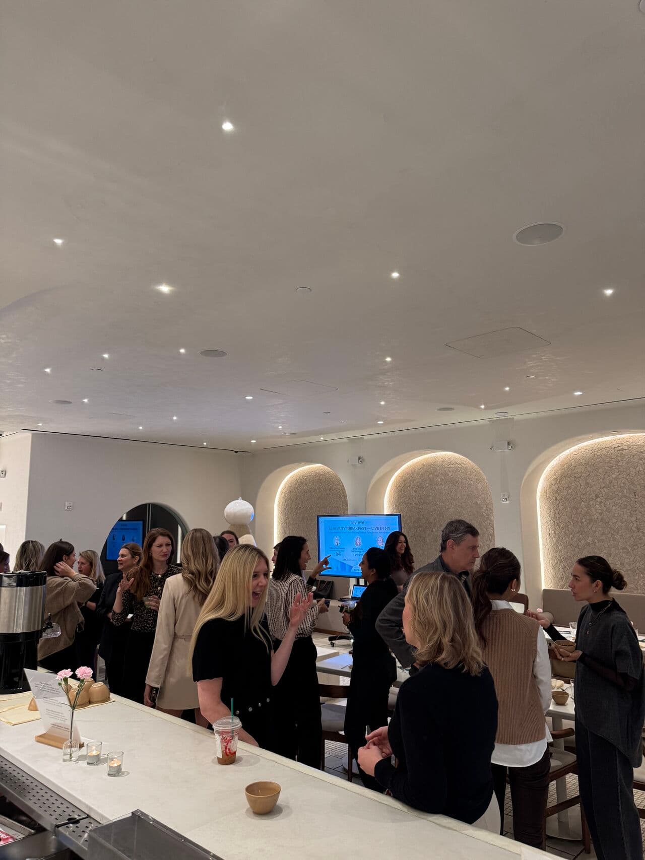 Guests networking at Revieve's AI Beauty Breakfast in New York, with a welcome screen reading “AI Beauty Breakfast — Live in NY”
