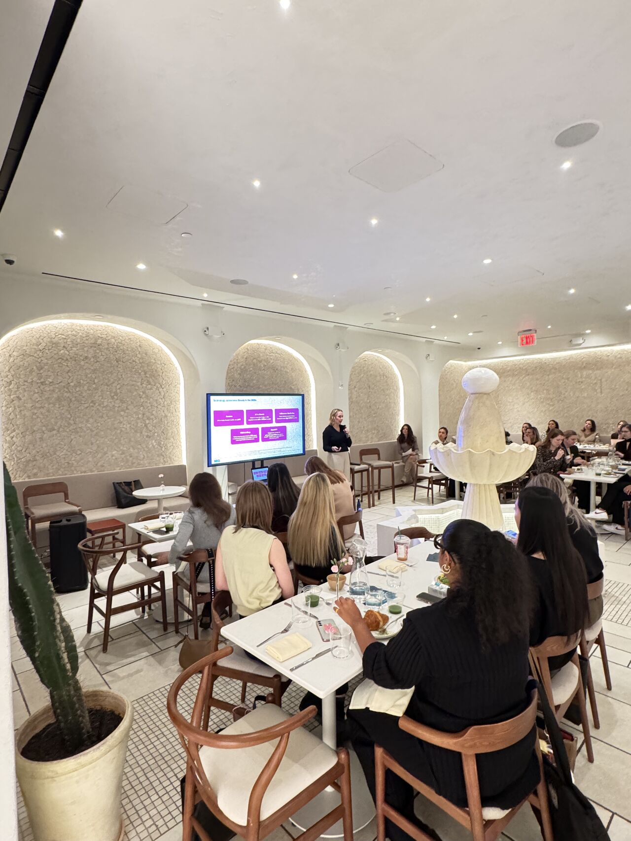 Attendees at Revieve's AI Beauty Breakfast in New York City watching a presenter speak in front of a slide